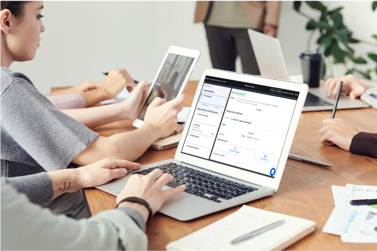 Woman sitting at a table with others using a laptop to build the meeting agenda on BoardPro