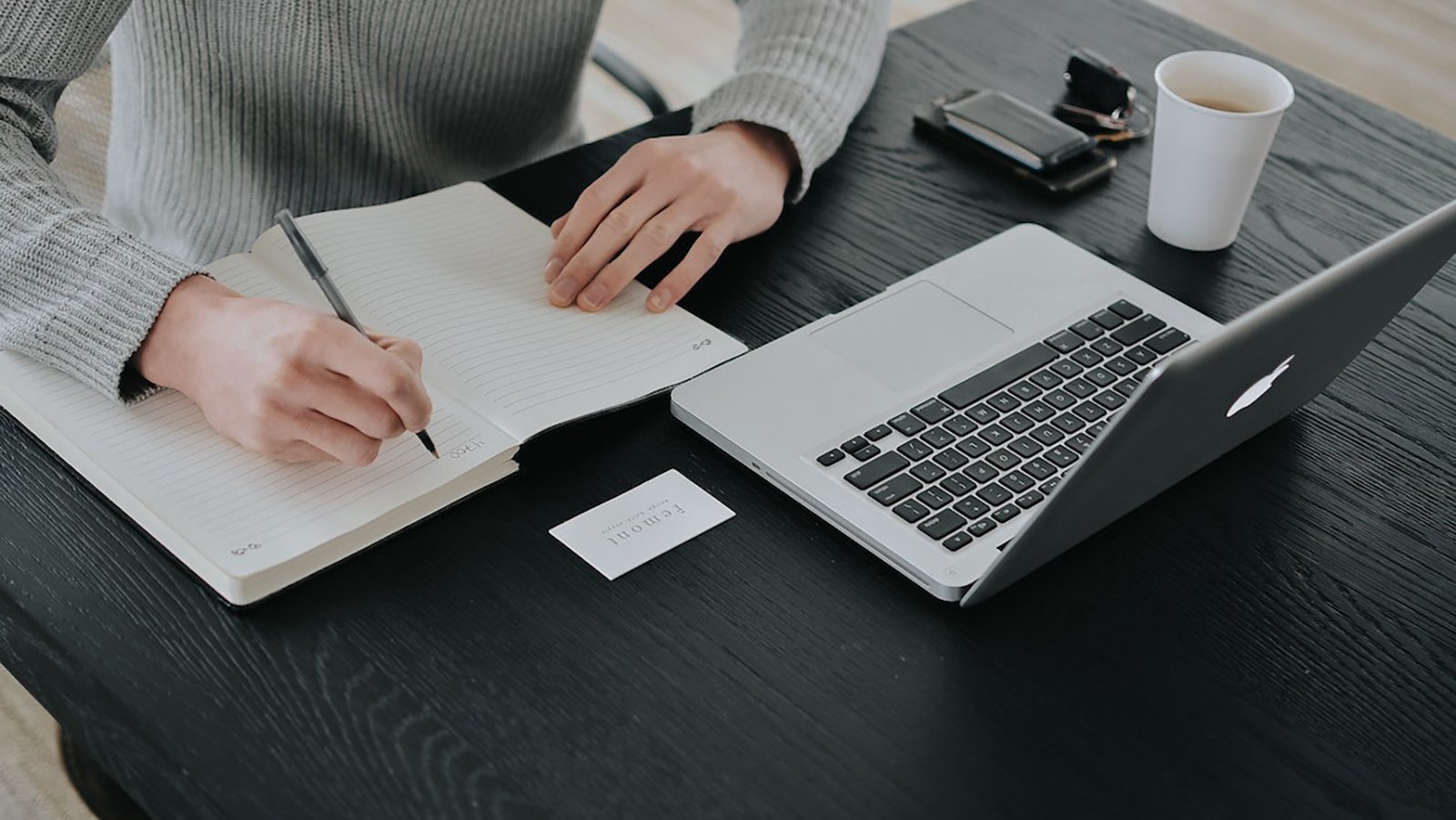 a laptop on a desk, with a person writing with a pen